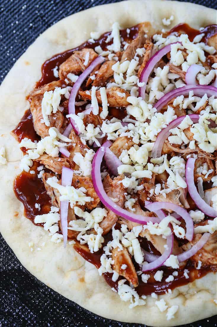 pizza topped with bbq sauce, cheese and red onions on a sheet pan