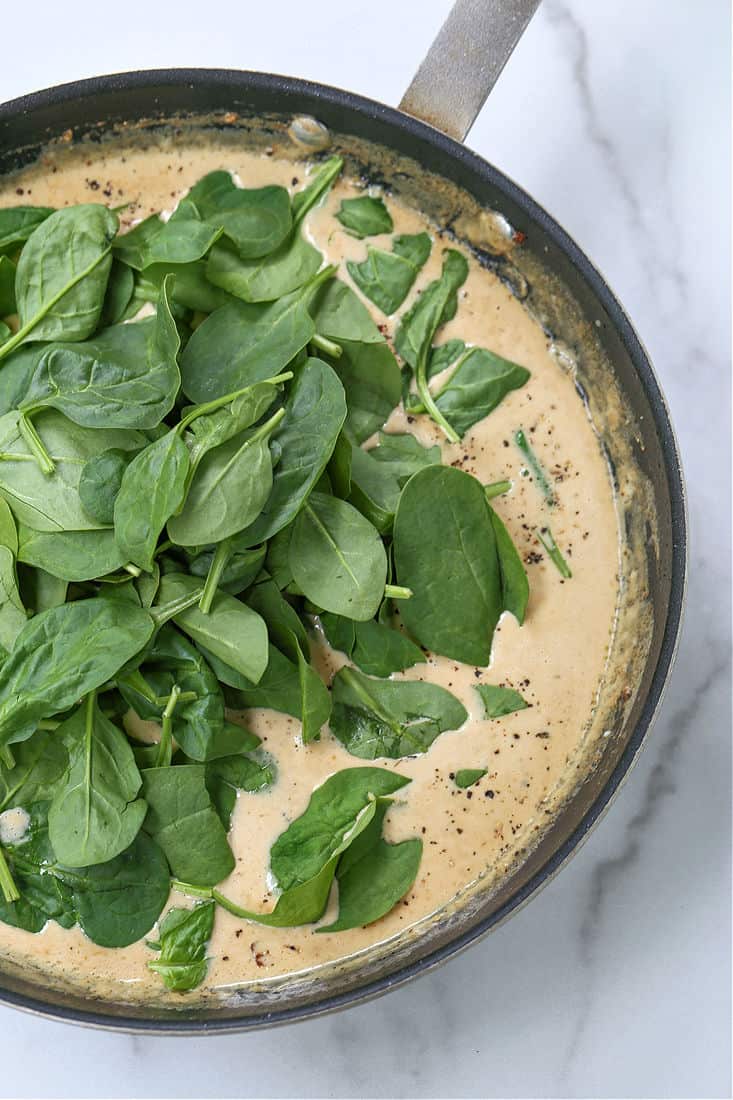 Fresh spinach added to a cream sauce in a skillet