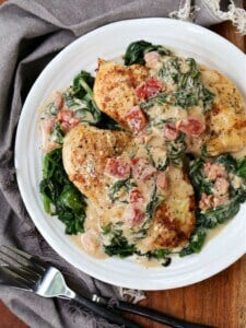 Chicken Florentine served on a plate with spinach and tomatoes in a creamy sauce.