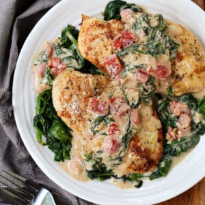 Chicken Florentine served on a plate with spinach and tomatoes in a creamy sauce.