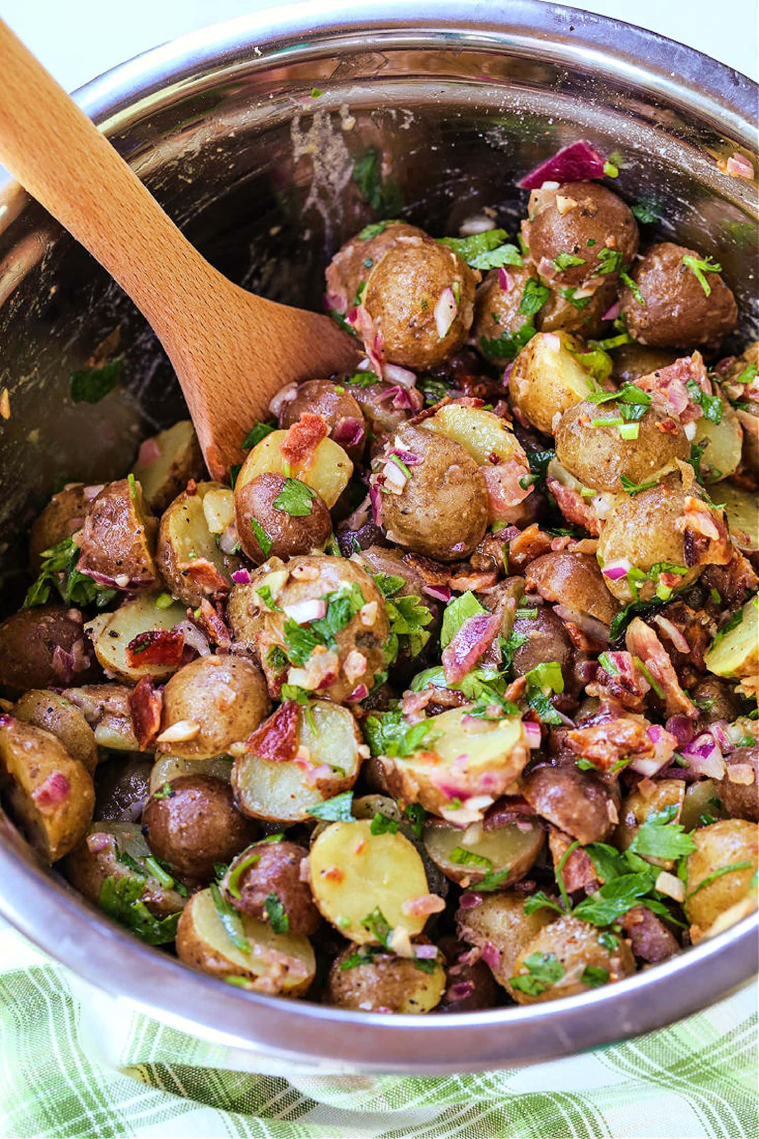 This Warm German Potato Salad is a classic party side! A no-mayo potato salad with tender potatoes, crispy bacon and a warm vinaigrette! wooden spoon in bowl with potato salad