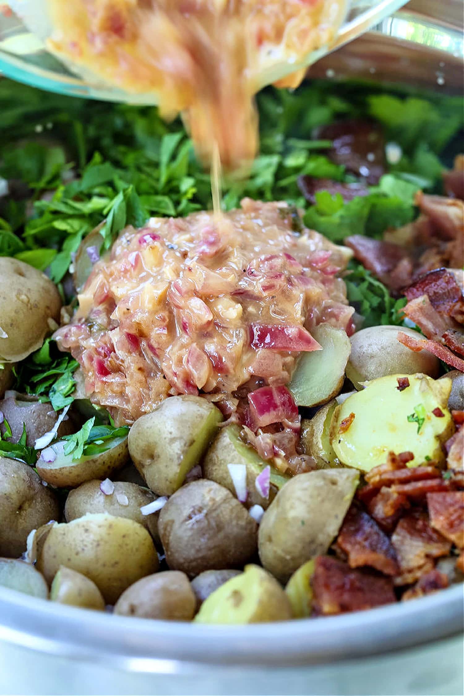 This Warm German Potato Salad is a classic party side! A no-mayo potato salad with tender potatoes, crispy bacon and a warm vinaigrette! warm vinaigrette being poured onto potato salad