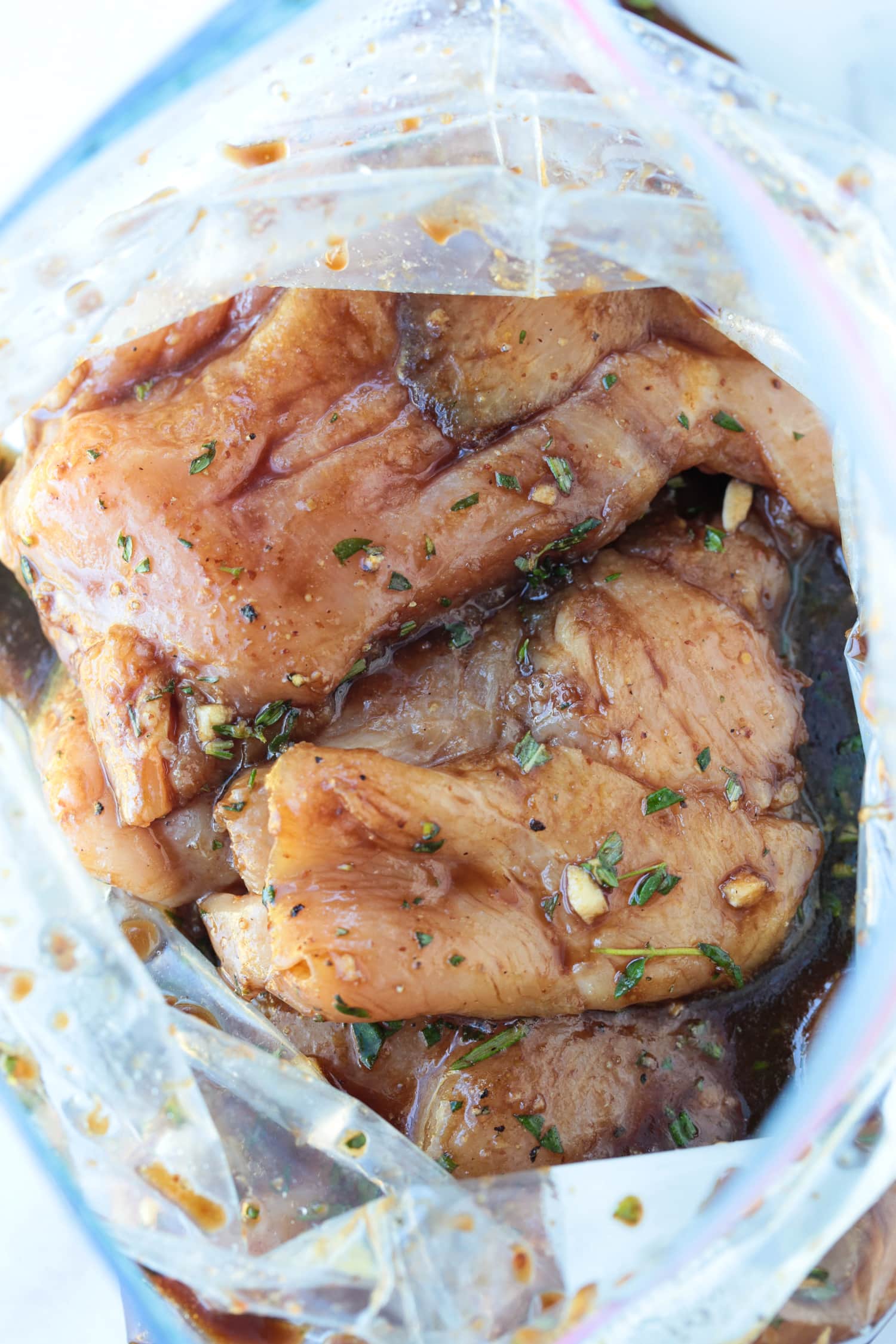 Our Balsamic Chicken Marinade is delicious on any cut of chicken! Tangy and sweet with fresh, vibrant herbs that flavor chicken wonderfully. chicken breasts marinating in a plastic bag