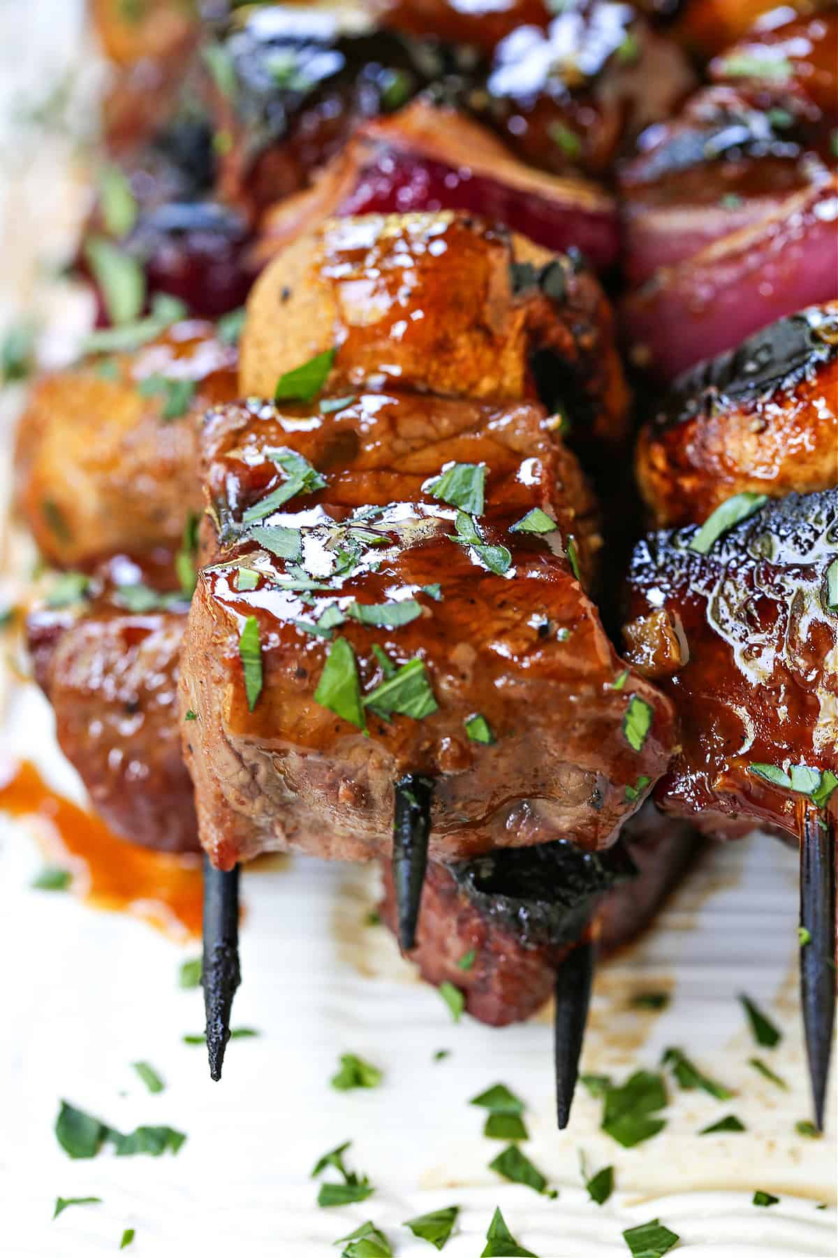 These Bourbon Steak Kabobs are always a hit! Grilled kabobs with tender steak and vegetables brushed with a brown sugar and bourbon glaze. close up of steak kabob with chopped parsley