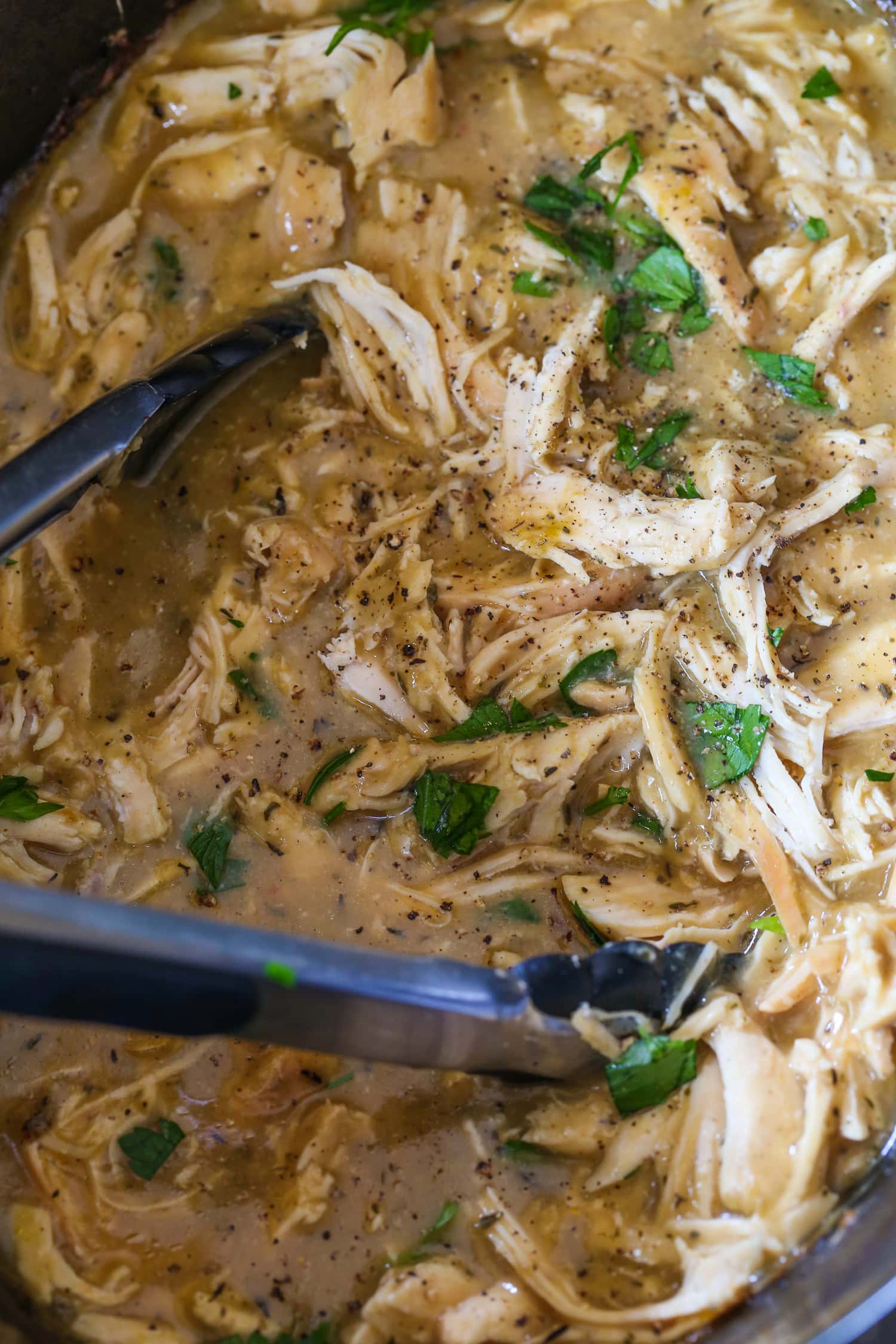 chicken and gravy in a slow cooker with tongs