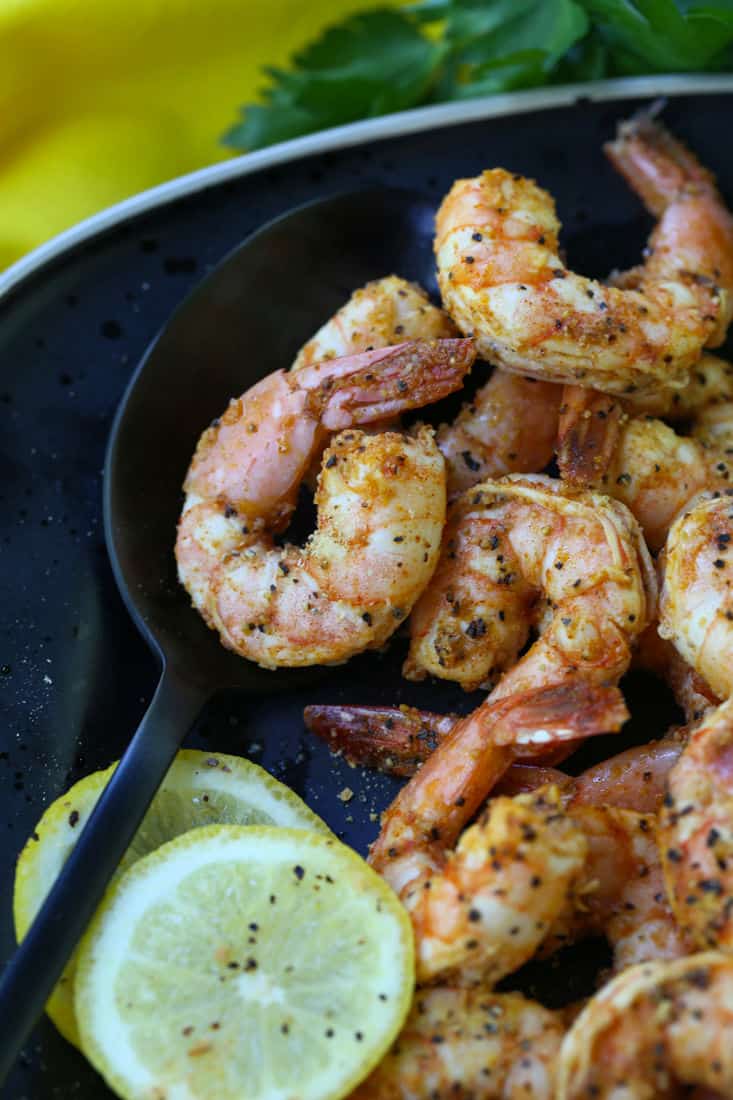 Shrimp on a black plate with a serving spoon