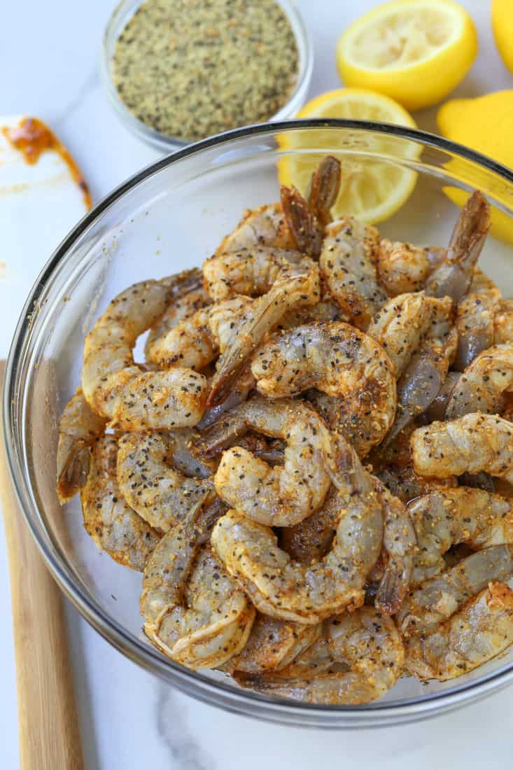 Shrimp in a bowl with lemon pepper seasoning and fresh lemons