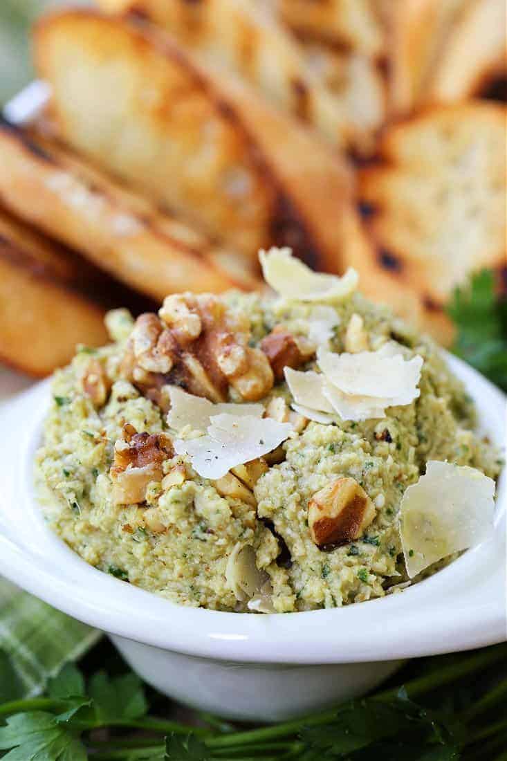 Pesto recipe with artichoke hearts, toasted walnuts and parmesan cheese in a serving bowl with toast