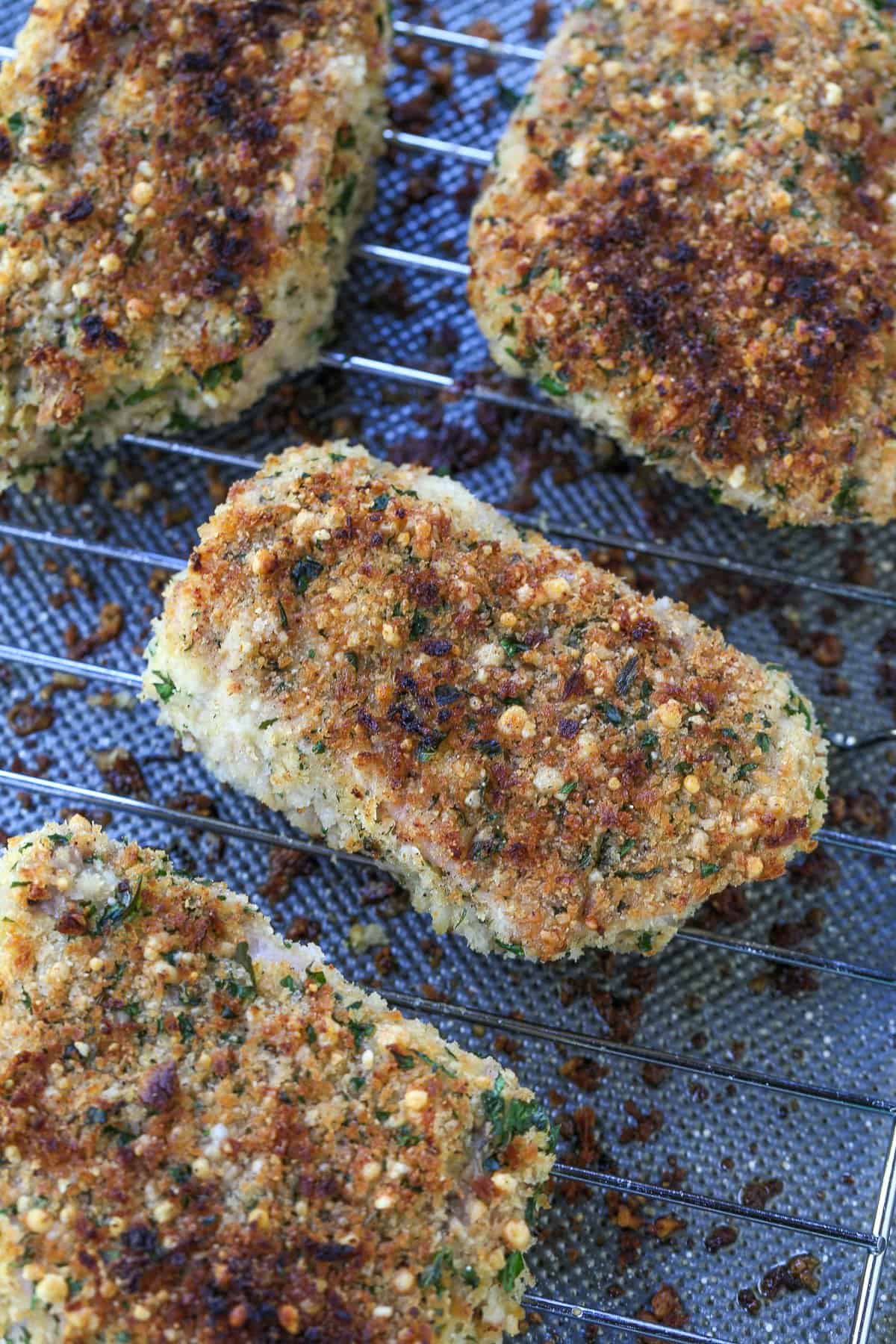 Crispy Baked Pork Chops have a panko breadcrumb and parmesan cheese crust that's so addicting. Crispy on the outside with a juicy inside. breaded pork chops on rack over baking sheet