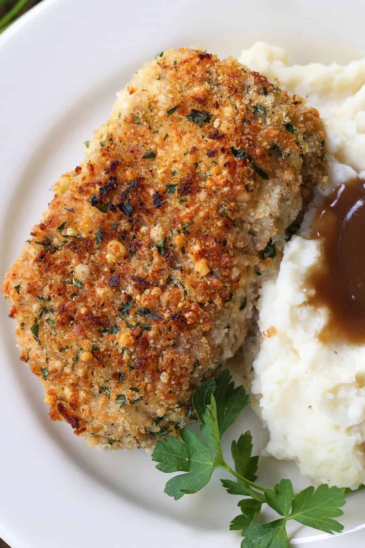 Crispy Baked Pork Chops have a panko breadcrumb and parmesan cheese crust that's so addicting. Crispy on the outside with a juicy inside. breaded pork chops on plate with mashed potatoes