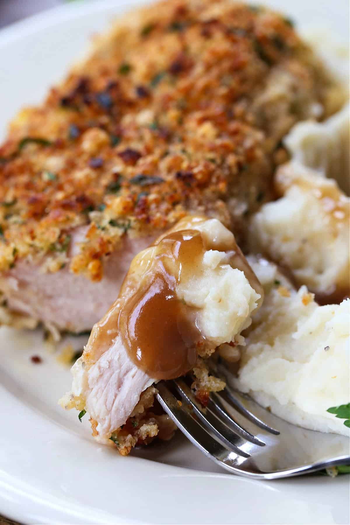 Crispy Baked Pork Chops have a panko breadcrumb and parmesan cheese crust that's so addicting. Crispy on the outside with a juicy inside. fork with bite of pork chop and gravy