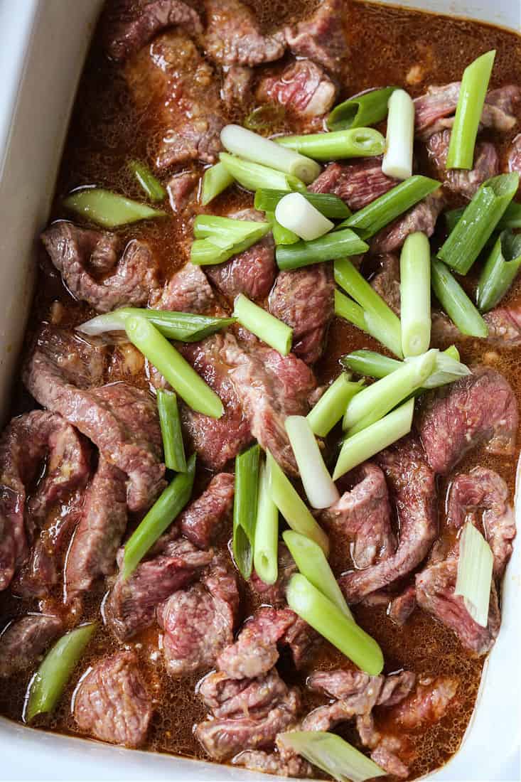 Sliced steak in a crock pot with scallions