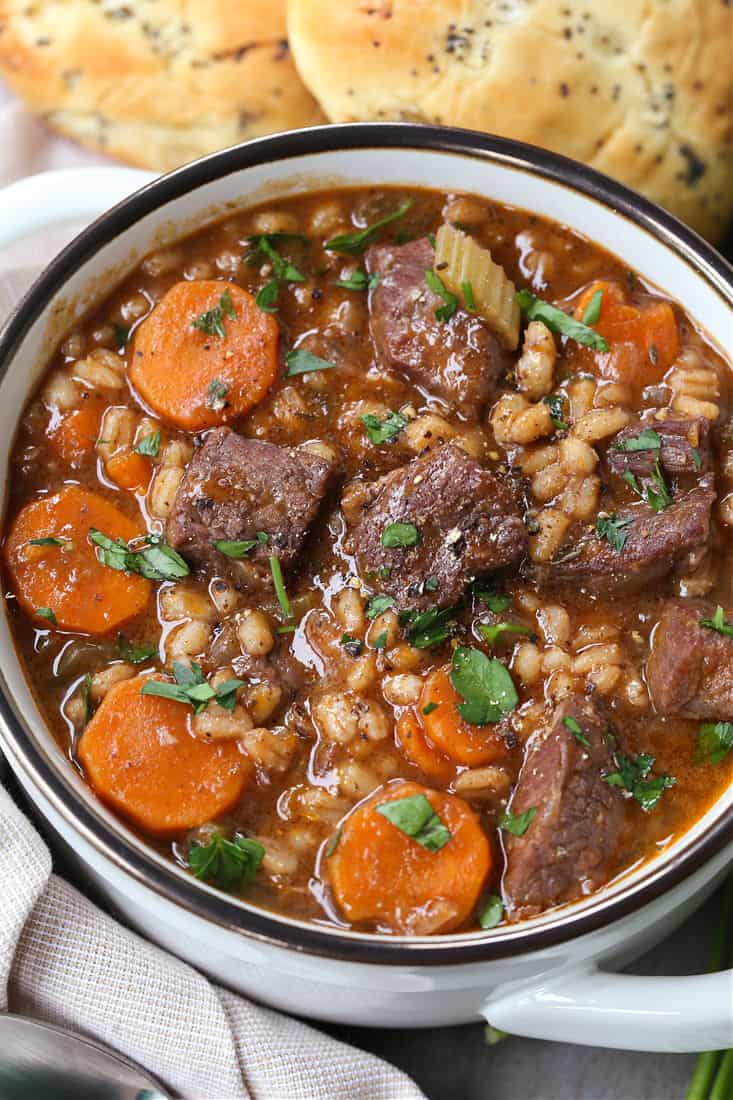 Beef Barley Soup in a bowl with napkin and rolls