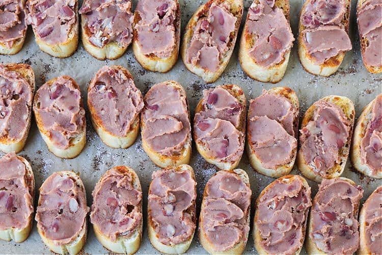 Refried beans on crostini to make cheesy taco crostini