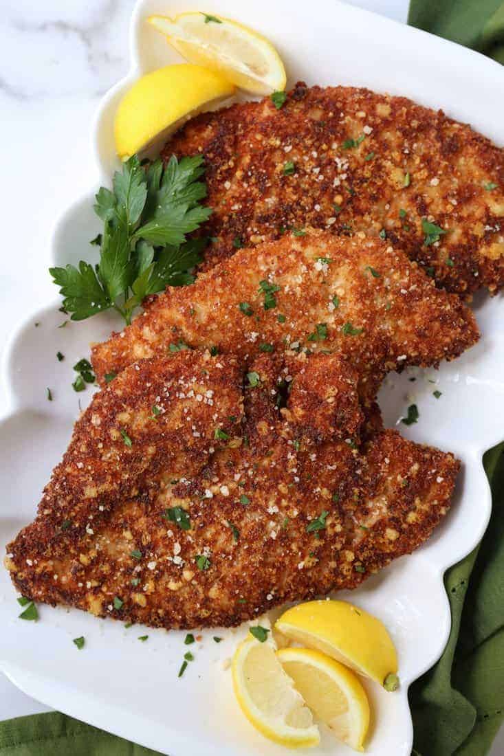 Breaded chicken cutlets with lemon wedges on a platter