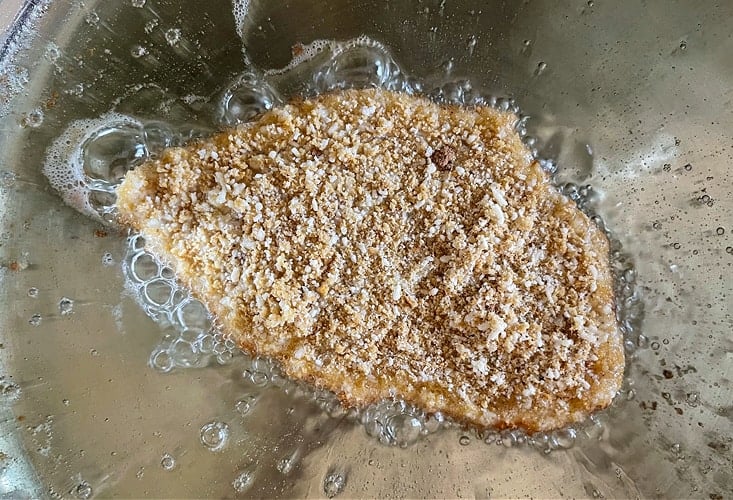 breaded chicken cutlet in a skillet with oil