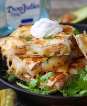 Tequila Shrimp Quesadillas stacked on a plate with tequila bottle