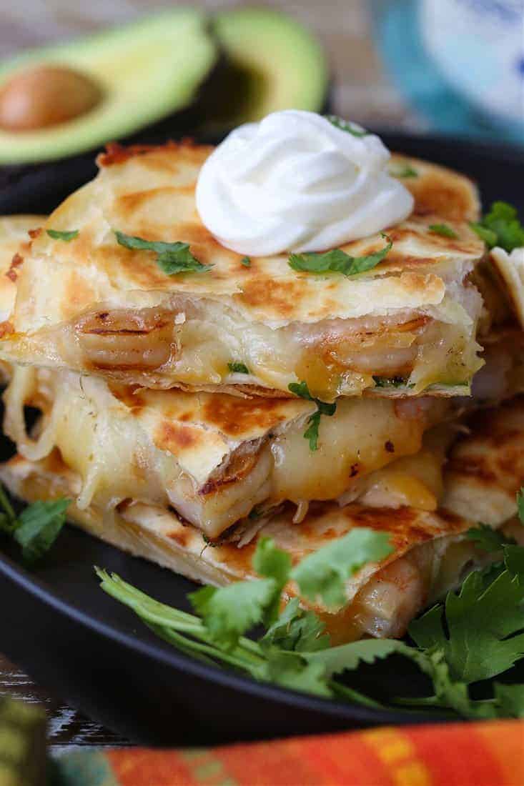 Tequila Shrimp Quesadillas stacked on a plate with sour cream