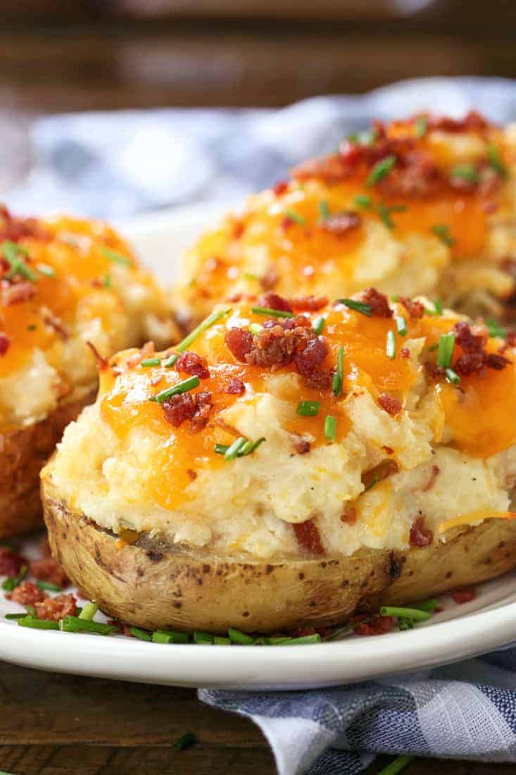 Twice Baked Potatoes are a delicious side dish that can be totally made ahead of time! Creamy, cheesy potato filling in a crispy baked skin! Twice Baked potatoes on a plate with checkered napkin