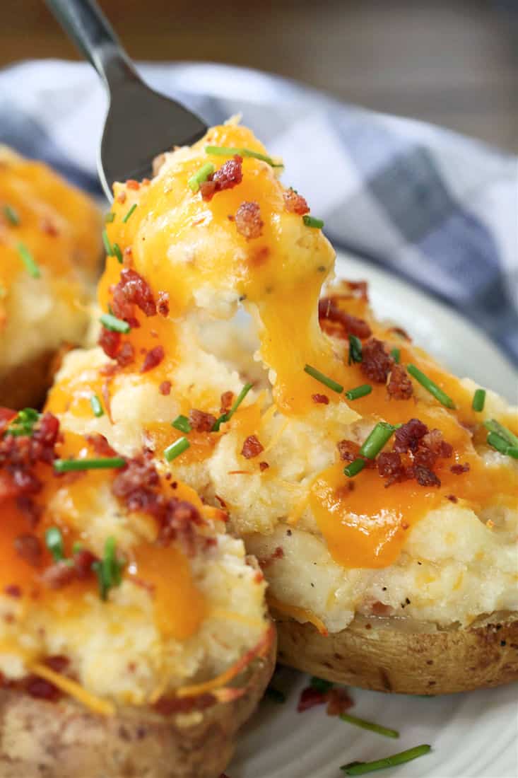Twice Baked Potatoes are a delicious side dish that can be totally made ahead of time! Creamy, cheesy potato filling in a crispy baked skin! A fork taking a bite of a twice baked potato