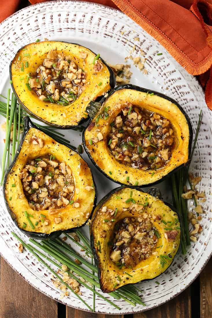 With a buttery texture and a golden caramelized crust, Acorn Squash with Brown Sugar and Walnuts features a sweet and nutty filling. Roasted Acorn Squash on a platter with chives for garnish.