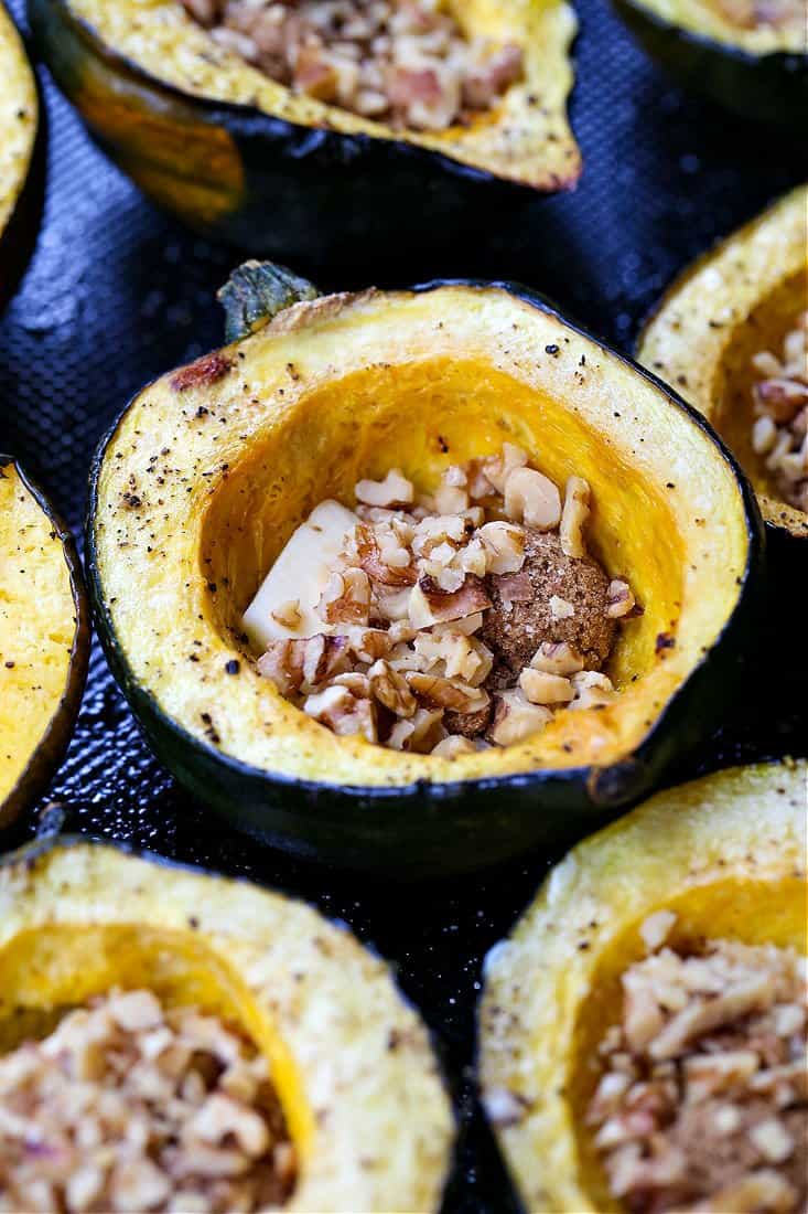 Acron squash on a baking sheet filled with butter, brown sugar and walnuts