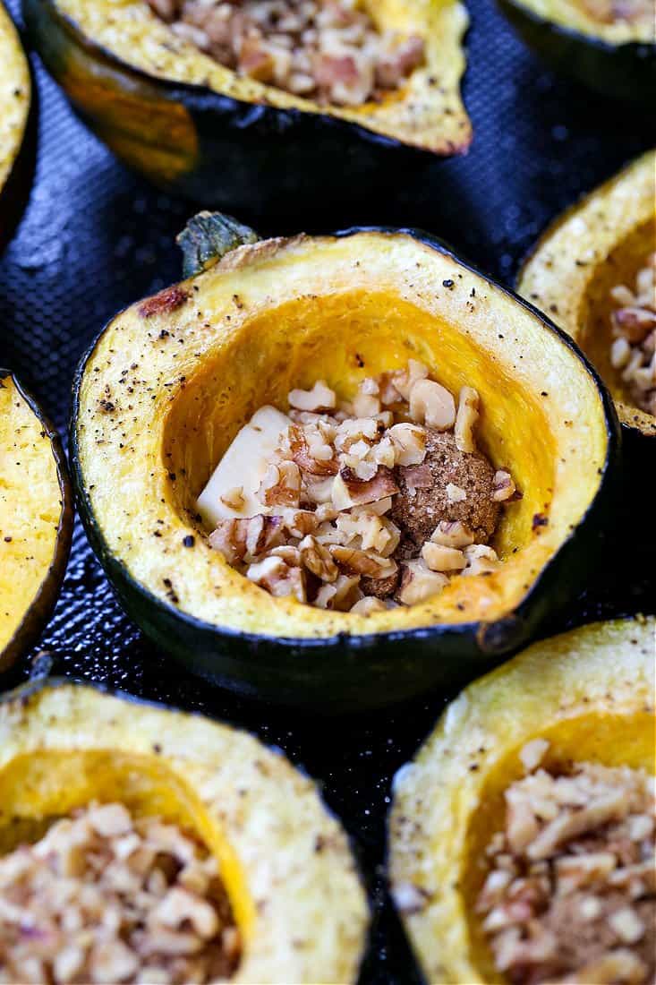 With a buttery texture and a golden caramelized crust, Acorn Squash with Brown Sugar and Walnuts features a sweet and nutty filling. Halved acorn squashes on a baking sheet filled with butter, brown sugar and walnuts.