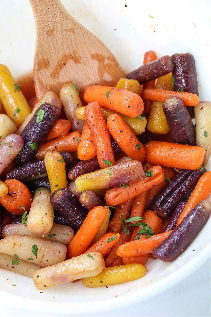 honey glazed carrots being tossed in a white bowl