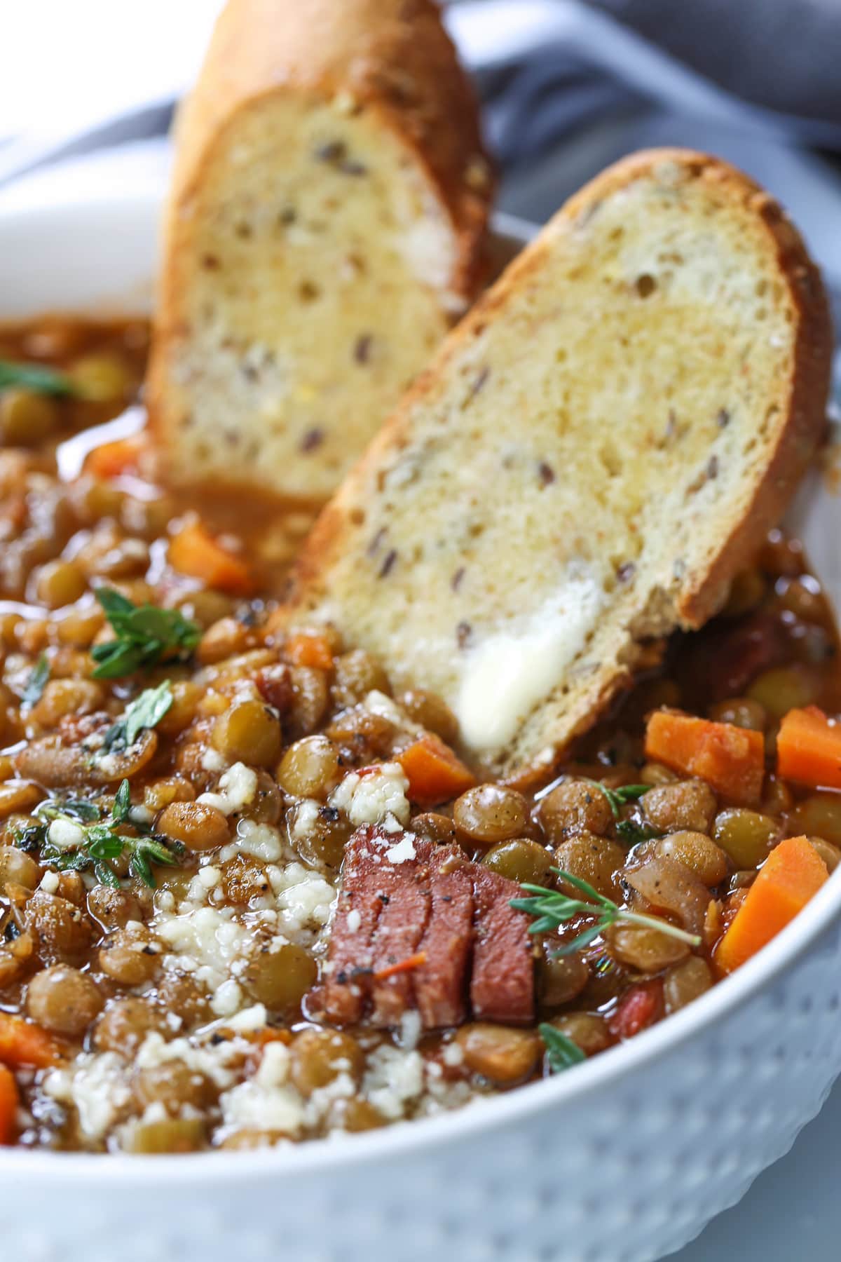 lentil soup with ham and vegetables in white bowl with toast