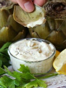 Artichoke leaf dipping into garlic aioli with lemon wedge on the side