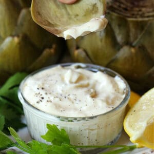 Artichoke leaf dipping into garlic aioli with lemon wedge on the side