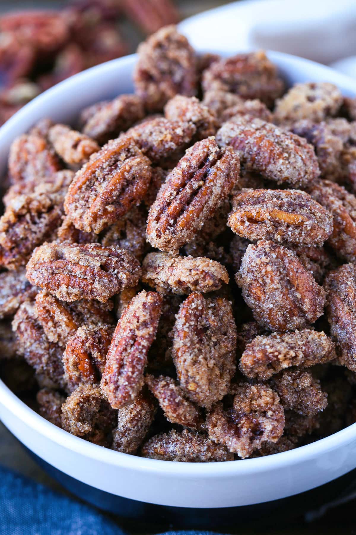 Our Candied Pecans Recipe is so addicting, you won't be able to stop eating them! A tasty snack recipe for parties, holidays and game days! close up of candied pecans in a white bowl