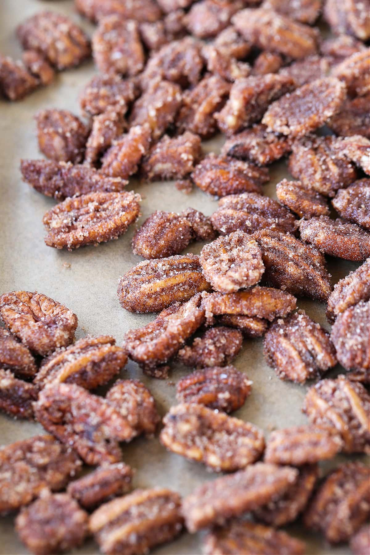 Our Candied Pecans Recipe is so addicting, you won't be able to stop eating them! A tasty snack recipe for parties, holidays and game days! glazed pecans on baking sheet with parchment paper