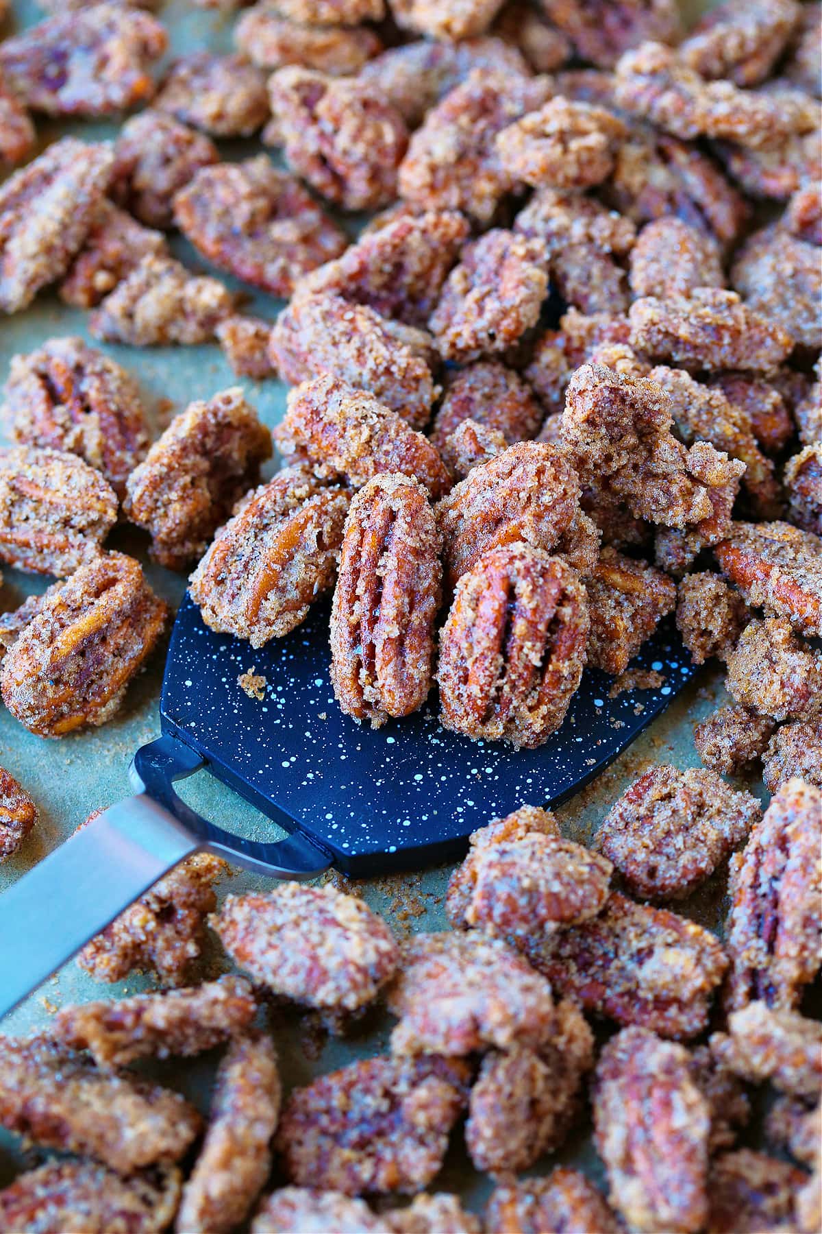 Our Candied Pecans Recipe is so addicting, you won't be able to stop eating them! A tasty snack recipe for parties, holidays and game days! spatula with candied pecans on baking sheet