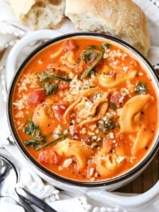 tomato tortellini soup in white bowl with bread on the side