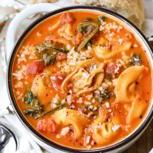 tomato tortellini soup in white bowl with bread on the side