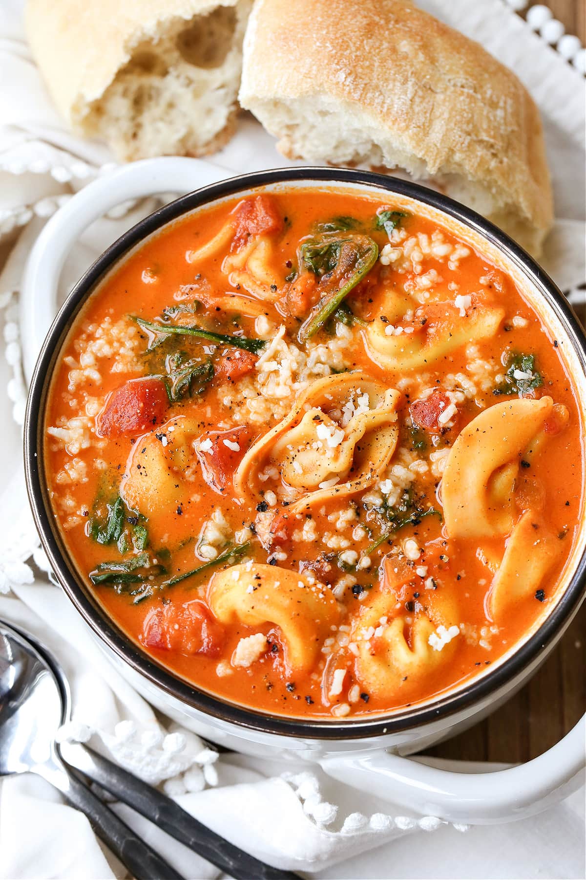 tomato tortellini soup in white bowl with bread on the side