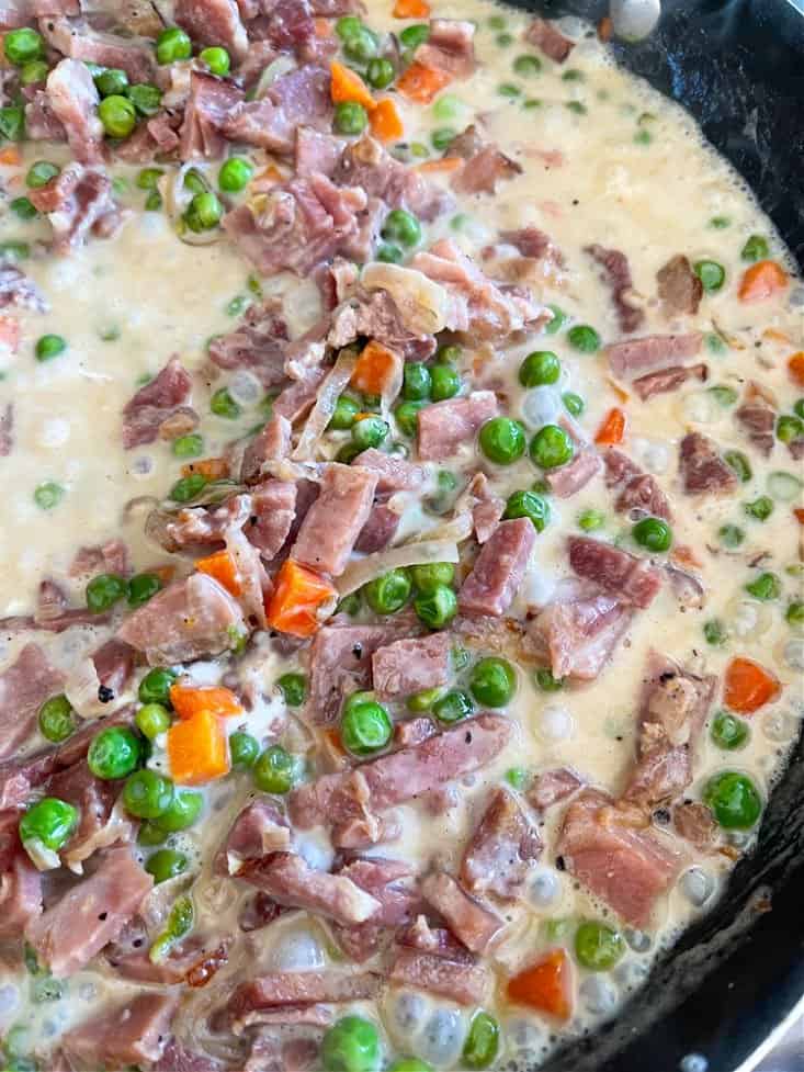 Vegetables and ham in a skillet with cream sauce