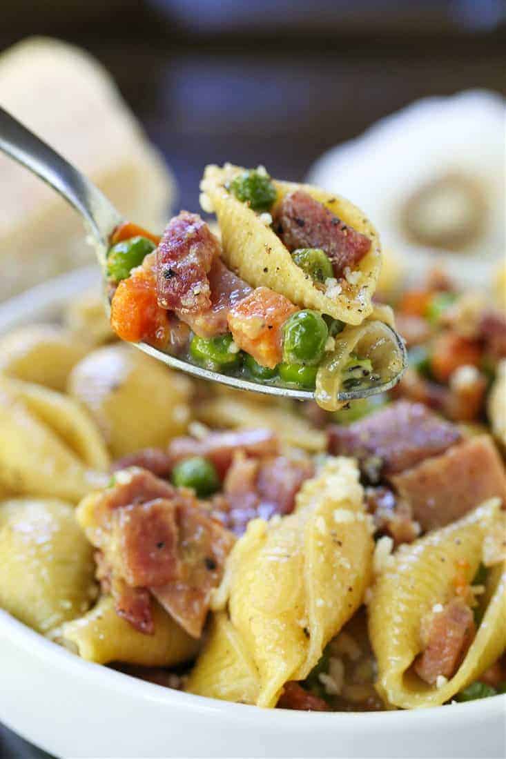 Pasta recipe with ham and peas on a spoon