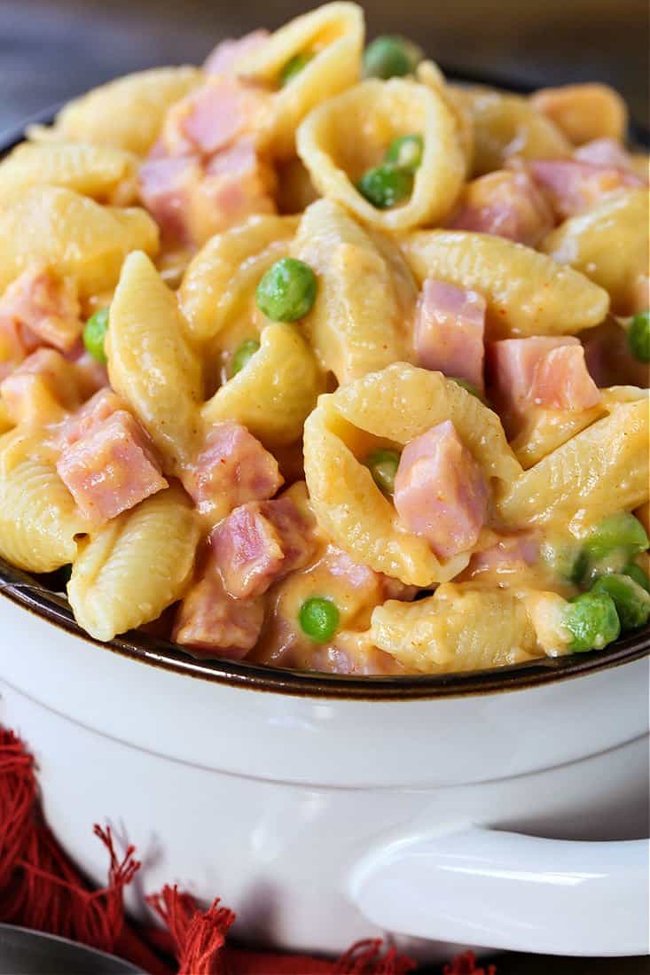 Cheesy Shells and Ham in a white bowl with peas