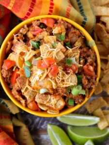 Frito Pie casserole in a bowl with limes and chips on the side