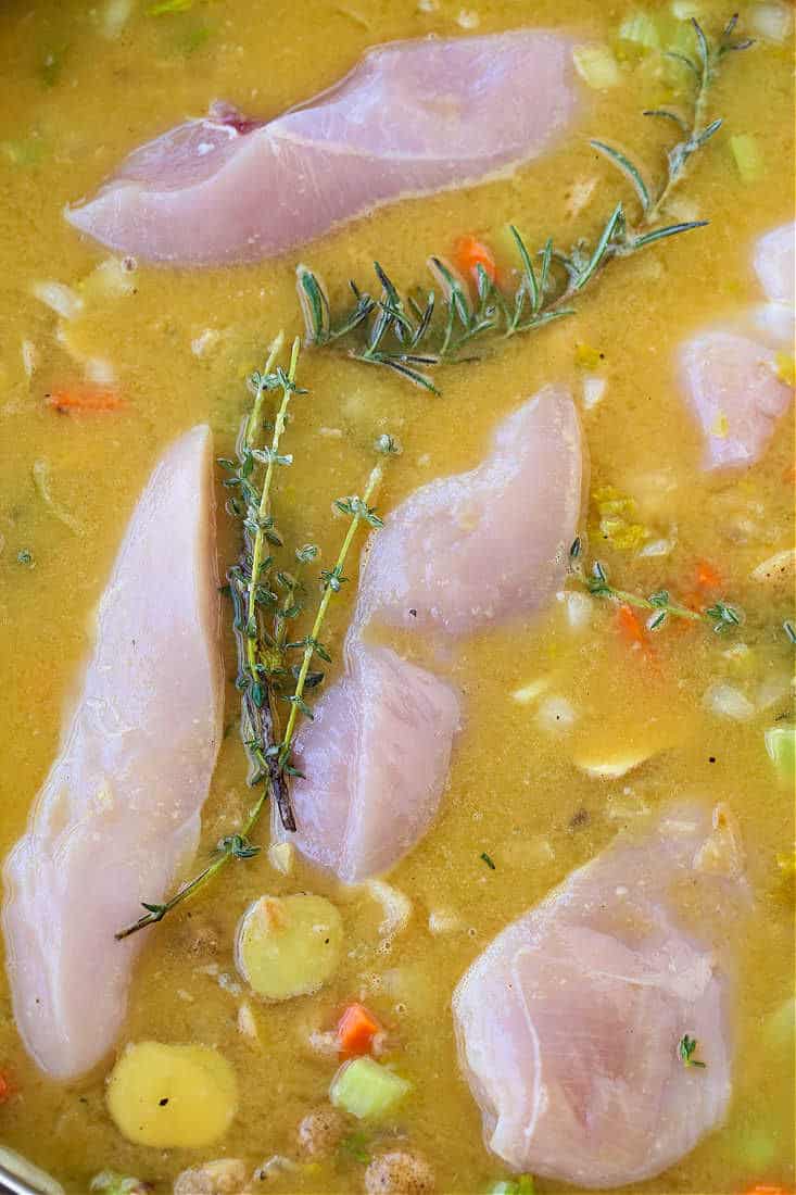 chicken breasts poaching in chicken broth with herbs and vegetables