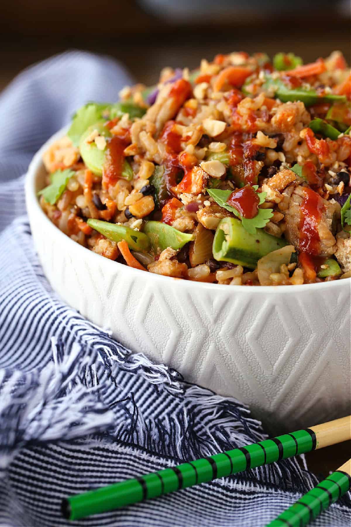Peanut Chicken Fried Rice is packed with tons of vegetables and lean ground chicken tossed with the most addicting, creamy peanut sauce! bowl of peanut chicken fried rice from the side with blue napkin