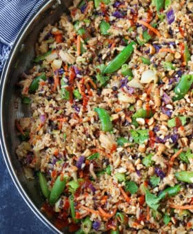 fried rice in a skillet with chopped snow peas and a sriracha drizzle