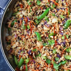 fried rice in a skillet with chopped snow peas and a sriracha drizzle