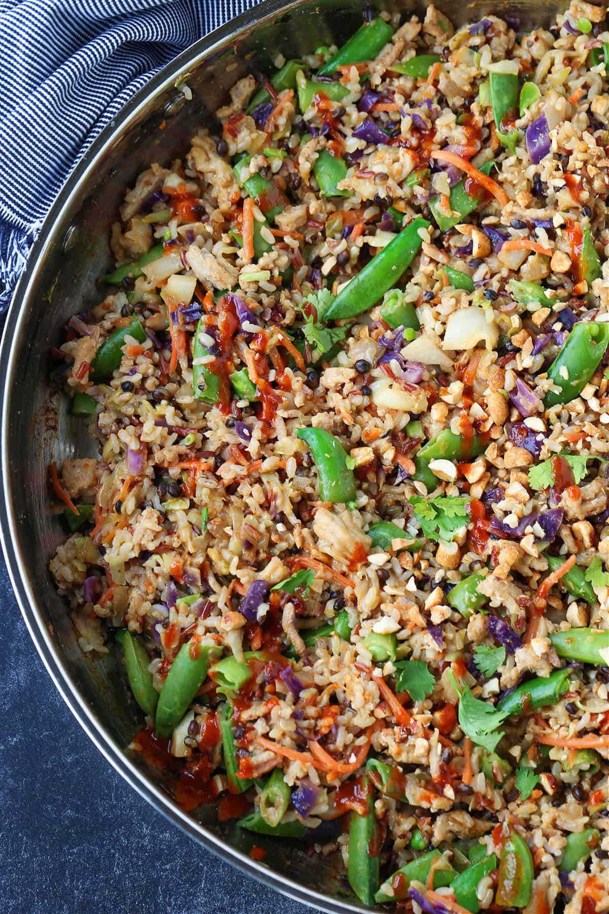 Peanut Chicken Fried Rice is packed with tons of vegetables and lean ground chicken tossed with the most addicting, creamy peanut sauce! fried rice in a skillet with chopped snow peas and a sriracha drizzle