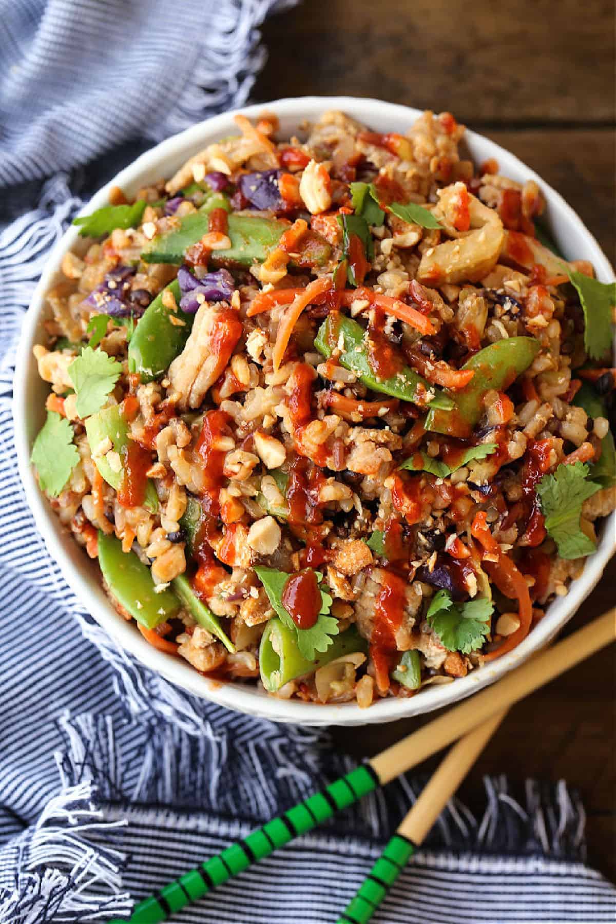 Peanut Chicken Fried Rice is packed with tons of vegetables and lean ground chicken tossed with the most addicting, creamy peanut sauce! fried rice in a bowl with sriracha drizzle