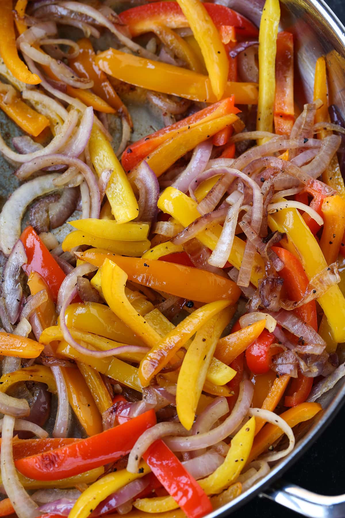 Our Steak Fajita Recipe turns any night into a party! Marinated flank steak with charred, sweet peppers and onions piled into warm tortillas. sliced peppers and onions in skillet for fajitas