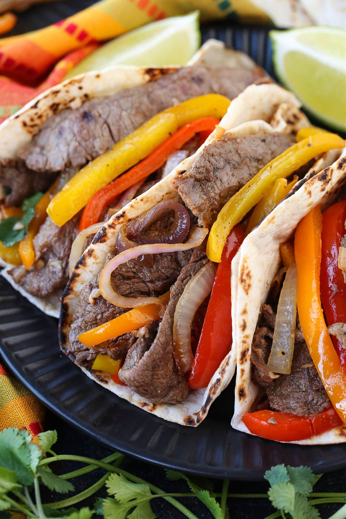 Our Steak Fajita Recipe turns any night into a party! Marinated flank steak with charred, sweet peppers and onions piled into warm tortillas. steak fajitas on black plate close up