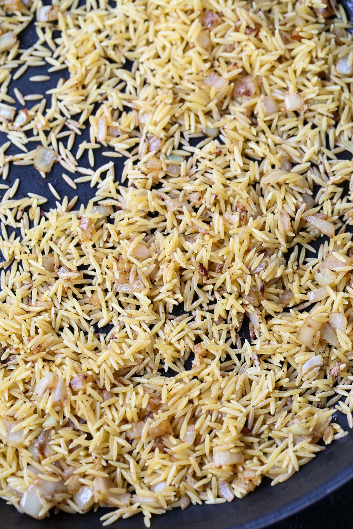 uncooked orzo in a skillet with onion